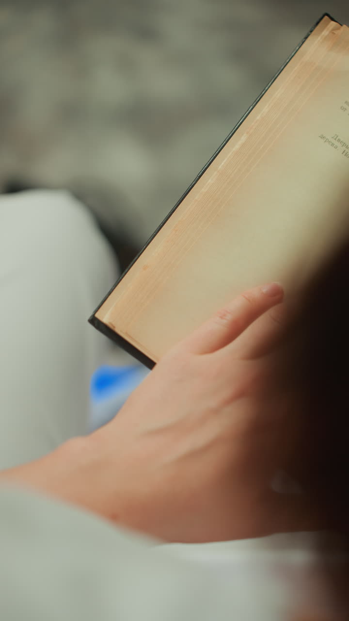 patient reading book during microcurrent therapy, adhesive electrode patch on wrist, relaxed hand turning aged pages, soft ambient lighting, quiet clinic chair, calm wellness atmosphere and gentle