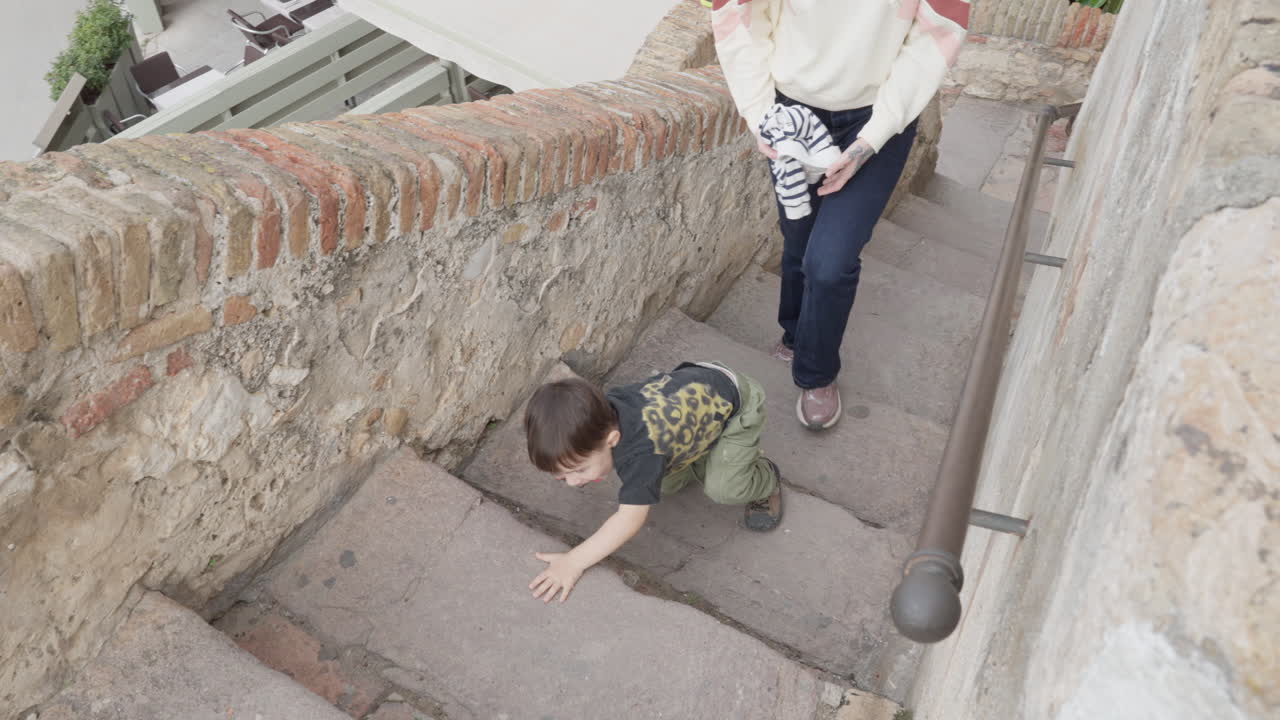 Toddler crawls up old stone stairs as his mother follows