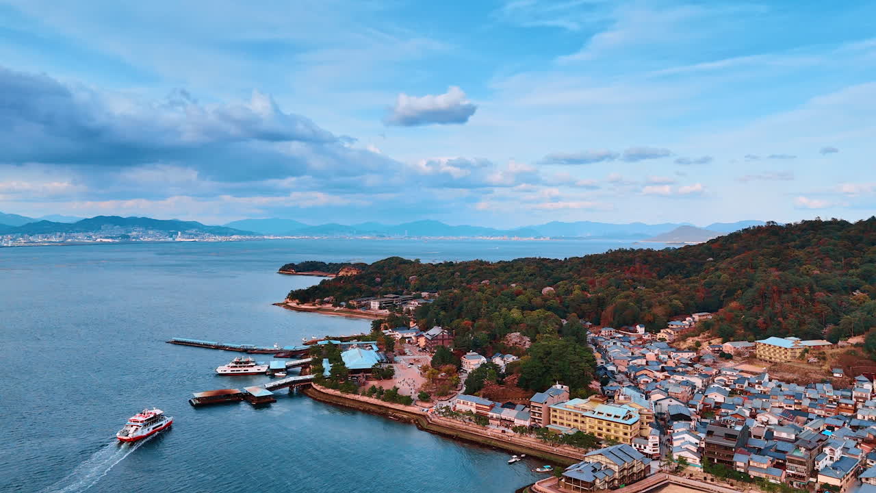 Flying closer to the shore of Japan Inland Sea built by multiple houses and covered by wooded mountains. Beautiful scenery of waterscape under the dramatic cloudscape.