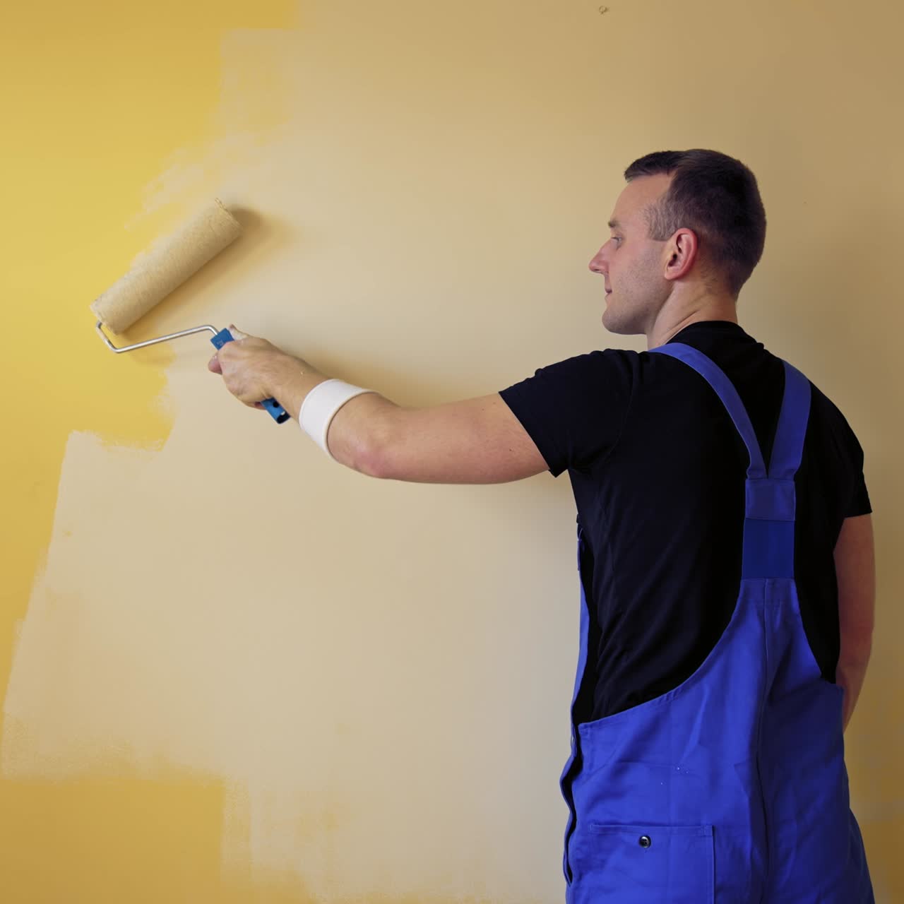Painter renewal room interior with a paint roller. Young builder is painting wall in the room. Worker changing color into lightsome in the apartment. Rear view