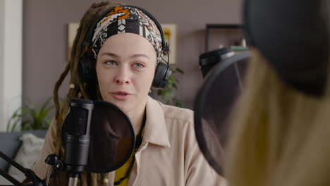 woman recording a podcast talking into a microphone with another woman sitting at desk