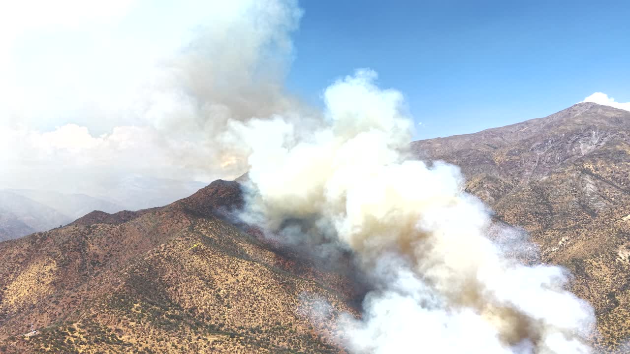Dronebillede af en aktiv skovbrand, der spreder sig gennem tør vegetation, med flammer og tyk røg, der stiger op over landskabet, hvilket viser miljøpåvirkning og naturkatastrofe. Chile og 4K