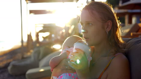 Mujer-Con-Hija-Relajándose-En-La-Playa-Y-Tomando-Una-Bebida-Helada