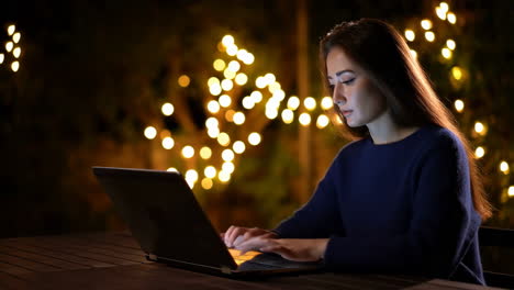 woman working on laptop outdoors at night with bokeh lights