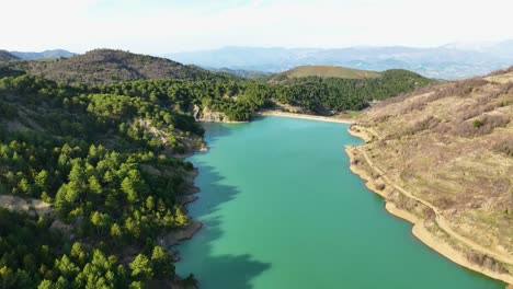 aerial shot revealing small lake on mountaintop with forest and hills nearby