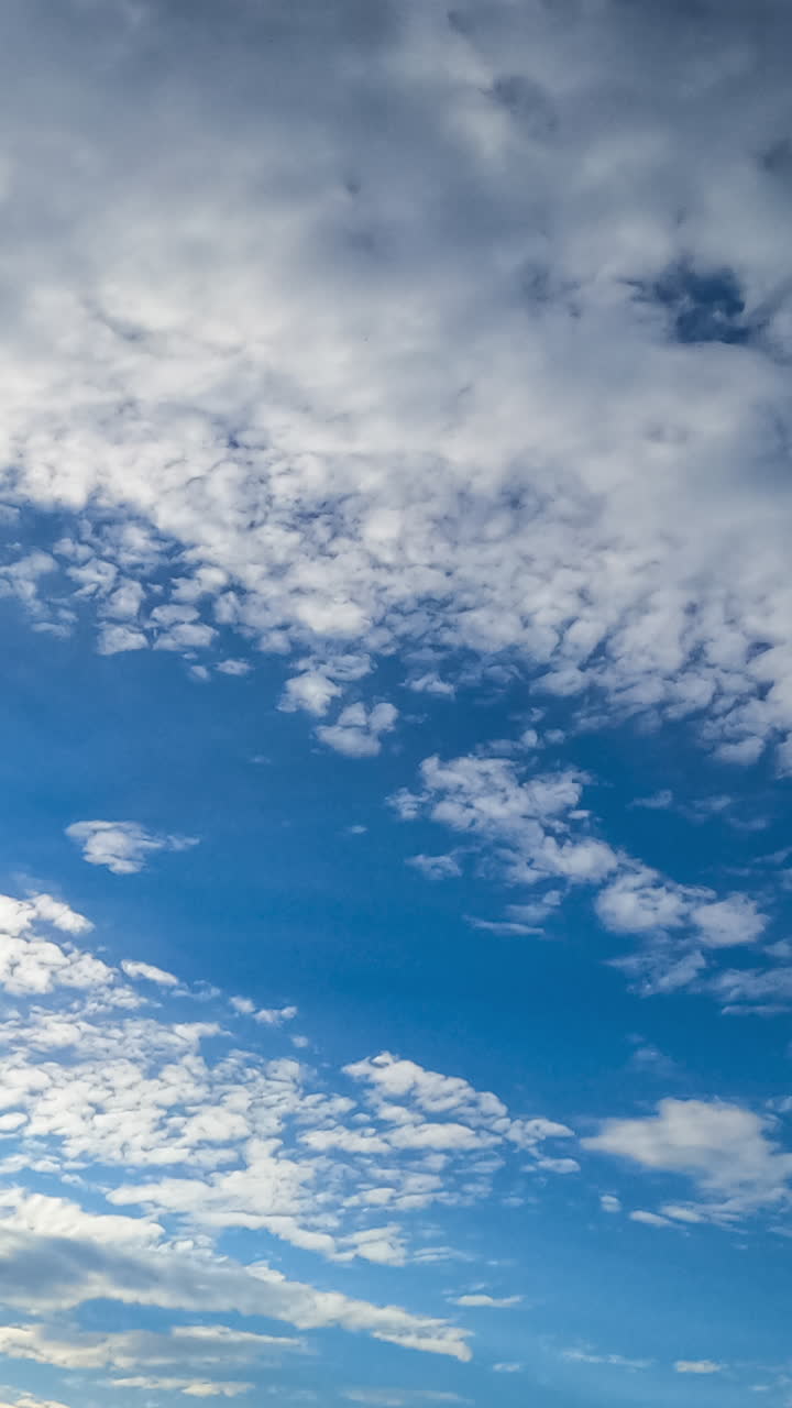 Beautiful light spindrift clouds fly away opening blue skies. Sun rays coming through the clouds. Timelapse view from below. Vertical video
