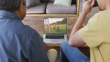 video de varios amigos hombres sentados en el sofá y viendo fútbol en la computadora portátil en casa