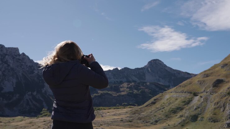 Una fotografa che scatta foto di paesaggi montani, vista da dietro, inquadratura fissa