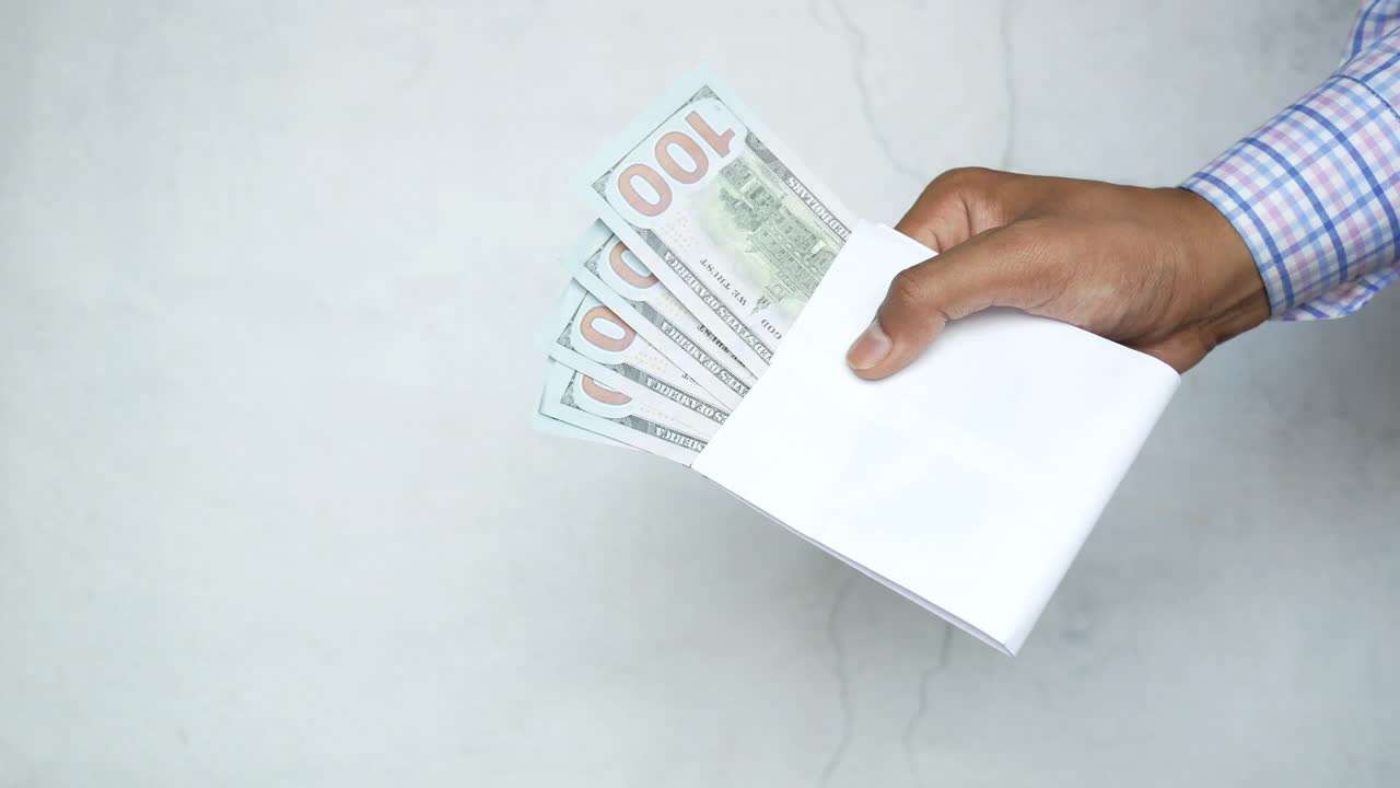 Hånd holder en hvid kuvert med amerikanske dollars indeni
