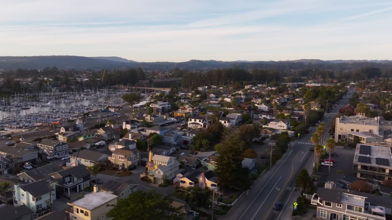 A drone shot circling a peaceful, beachside Santa Cruz California community with expensive residential houses and short term rentals next to the small craft harbor at sunset
