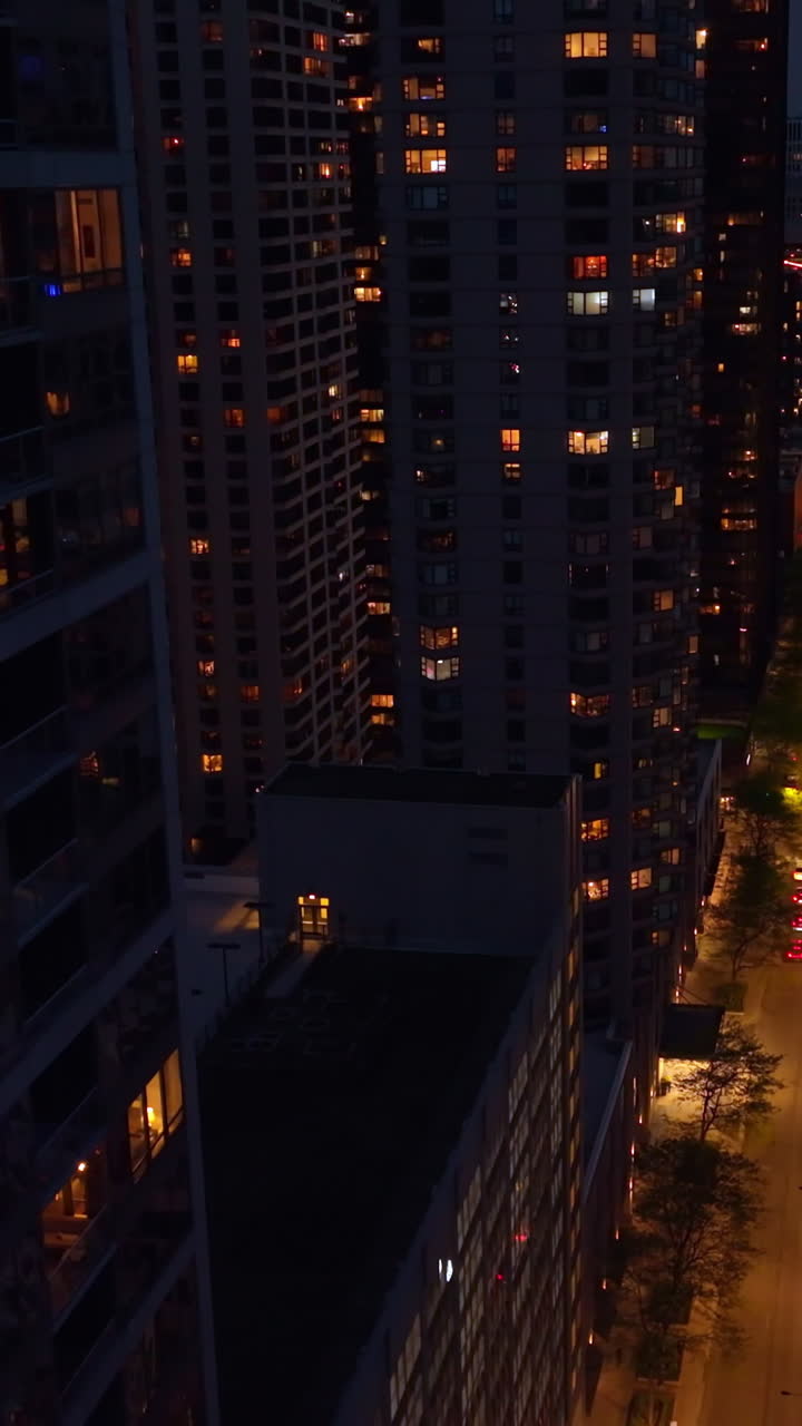 Well-lit street of Chicago downtown at night. Drone footage descending among the stunning skyscrapers over the busy road. Vertical video