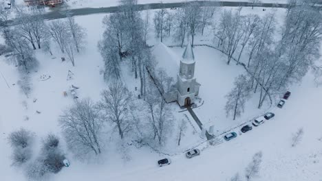 winter blankets a small church and surrounding cars in a quaint renda village , aerial birdseye orbit view