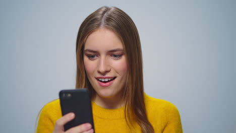 Retrato-De-Una-Atractiva-Mujer-Sonriente-Usando-Un-Teléfono-Inteligente-Sobre-Fondo-Gris.