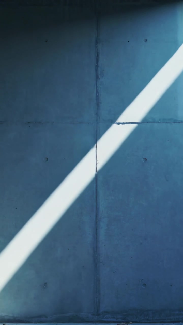 Video verticale: Raggio di sole che attraversa da una fessura una parete in cemento nella stanza, rivelando giunture e ancoraggi.