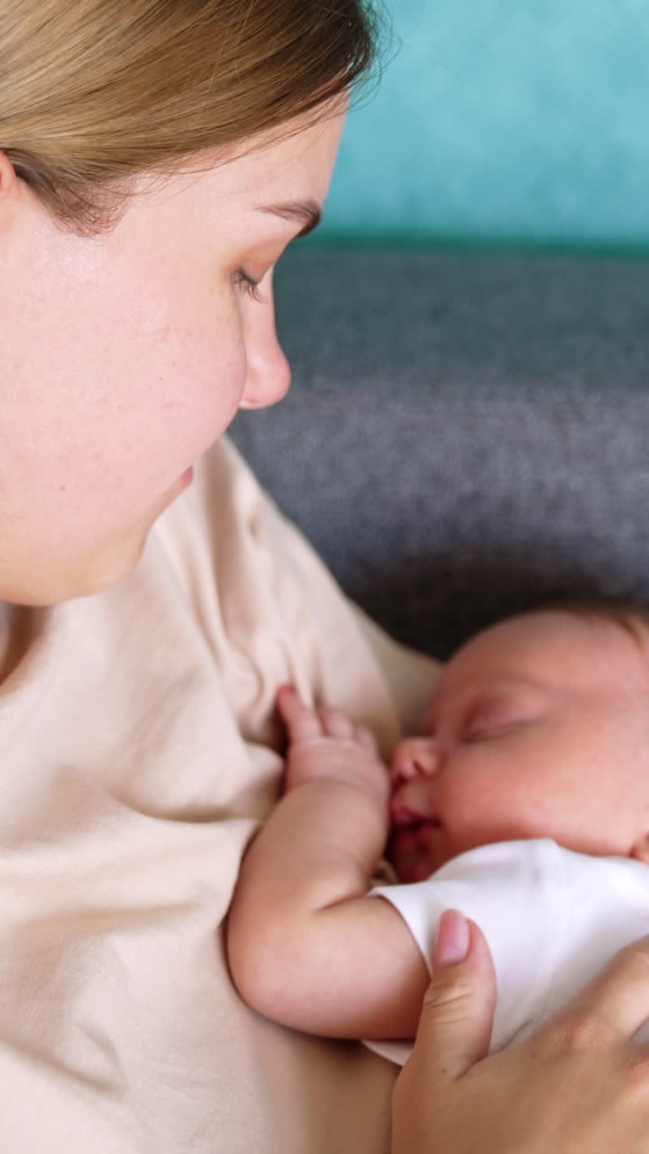 Blond Caucasian woman holding her sleeping newborn. Mom touches her child's ear tenderly. Close up. Vertical video