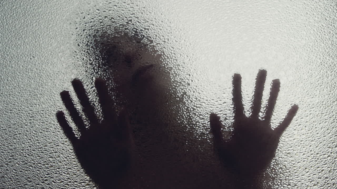 A female silhouette behind the frosted window touches the glass slowly