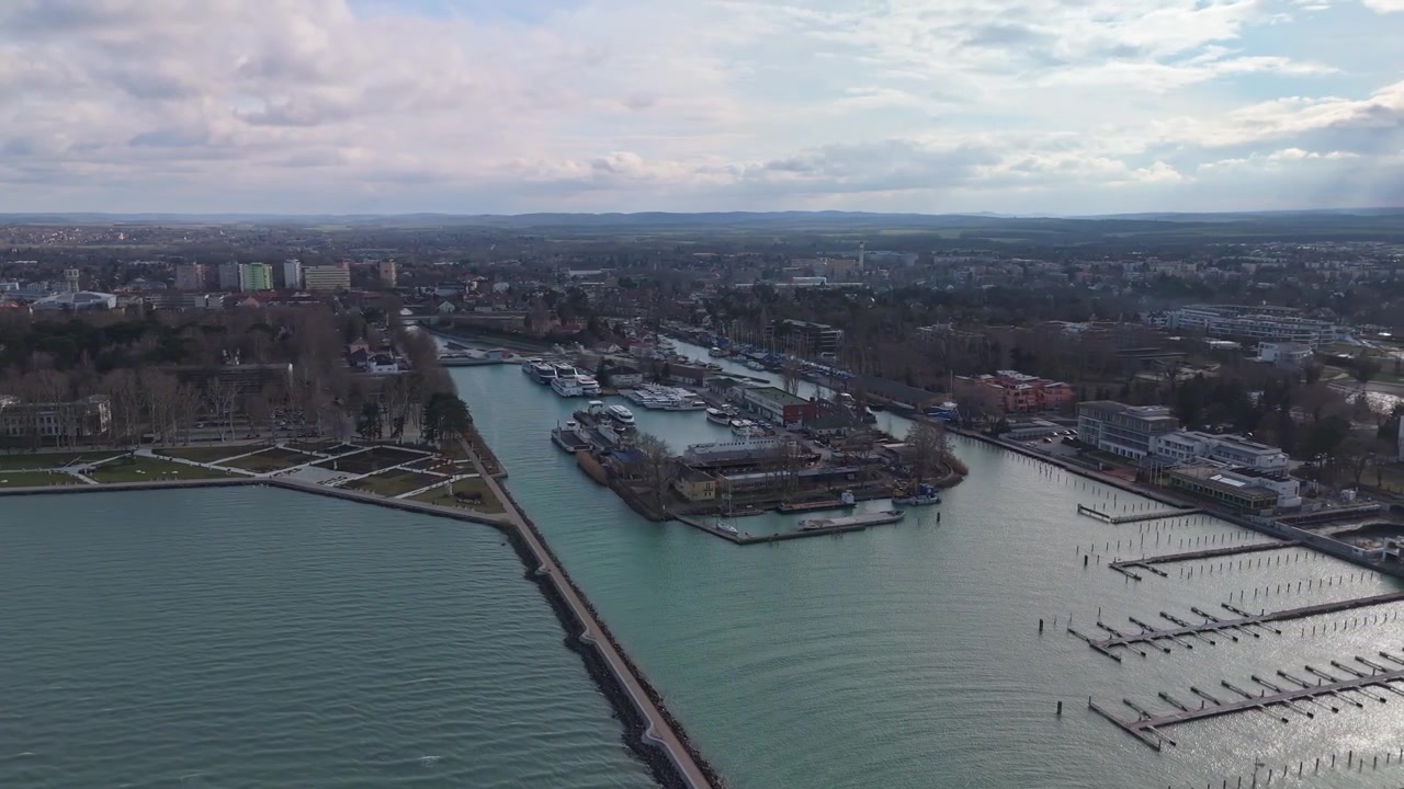 A Siófok, una vista aerea riprende barche e traghetti ormeggiati lungo il porto del Lago Balaton, accanto alla costa urbana con hotel, appartamenti e un cielo invernale nuvoloso.