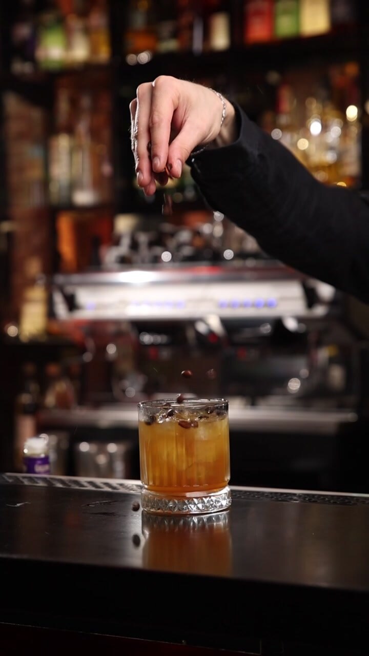 Barman professionista che guarnisce un cocktail ambrato con chicchi di caffè