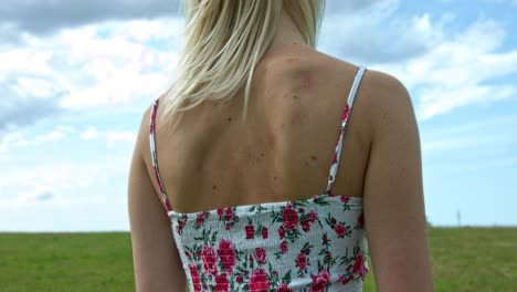 A-close-up-of-a-woman-facing-the-view-of-the-green-grass-and-the-cloudy-blue-sky