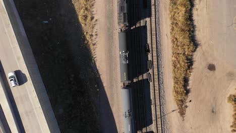 an idle train rests along a busy freeway