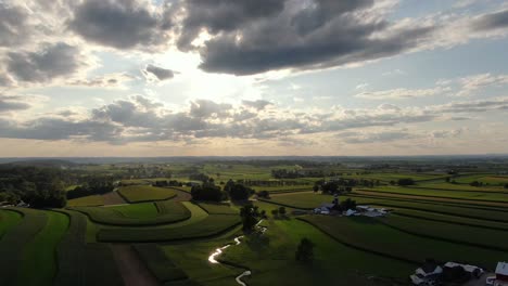 Magnífica-Toma-Aérea-Cinematográfica-Del-Cielo-Lleno-De-Nubes-Retroiluminadas-Durante-La-Puesta-De-Sol,-Hermosos-Reflejos-En-El-Corte-Del-Arroyo-A-Través-De-Los-Campos-Rurales