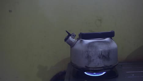 metal colored kettle with boiling water on a stove in poor kitchen