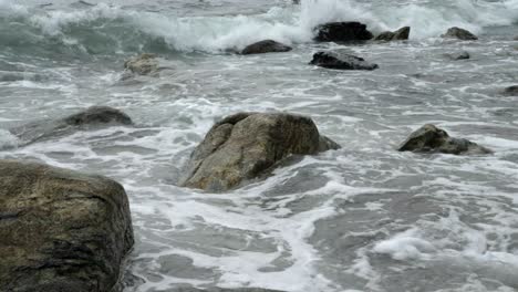 low angle view across stones poking out from ocean waves on rocky shoreline