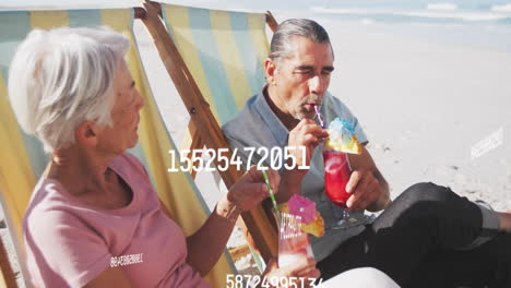 Sipping-tropical-drinks-on-beach,-couple-relaxing-with-numbers-animation-over-scene