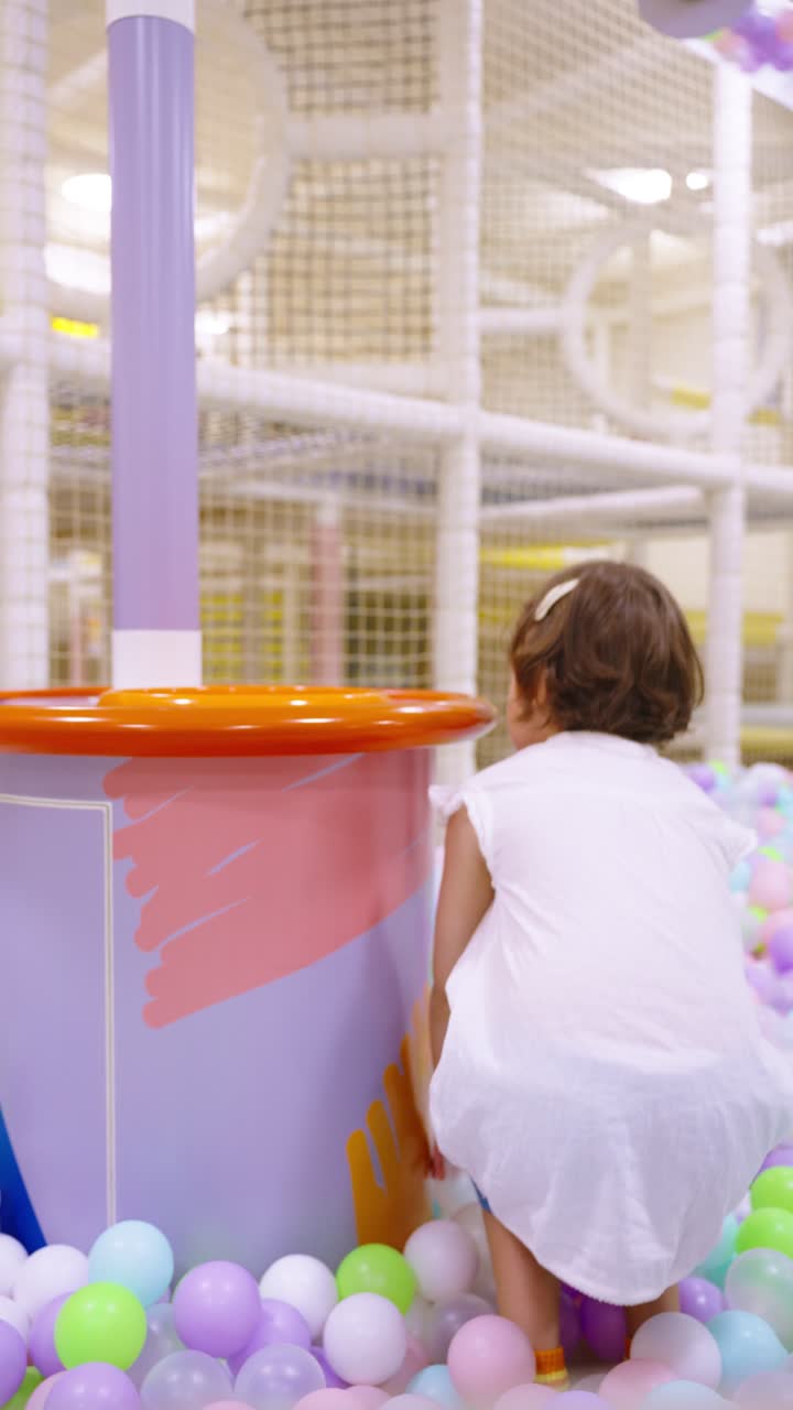A five-year-old girl collects colorful balls in a bucket at an indoor play area - slow motion, vertical