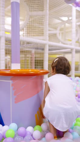 a five-year-old girl collects colorful balls in a bucket at an indoor play area - slow motion, vertical