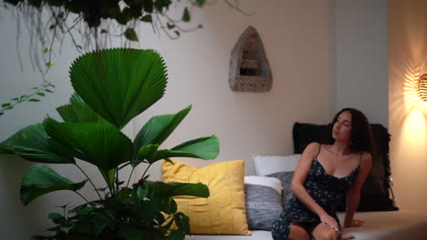 young woman relaxing and stretching on a daybed with green house plants all around, natural lifestyle eco living design