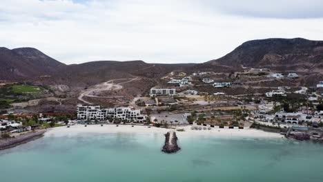 Vista-Aérea-Frente-Al-Destino-Soñado-Frente-A-La-Costa-De-Playa-El-Caymancito-En-Baja-California-Sur,-México-Con-Vista-Al-Agua-De-Mar-Turquesa,-Hermosa-Playa-De-Arena-Y-Edificio-De-Hotel-Para-Turistas