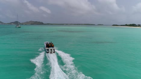 AERIAL-VIEW-Coast-Guard-boat-FROM-BEHIND-SAIL-on-turquoise-sea-water,-LOS-ROQUES-VENEZUELA