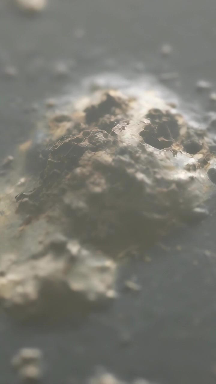Vertical video: Moving camera closing in on mound on gray slab revealing specks and highlights