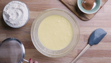 preparar el tamiz para tamizar la harina en un bol con ingredientes líquidos mezclados