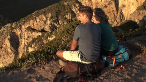 couple of backpack tourists taking break, sitting at cliff