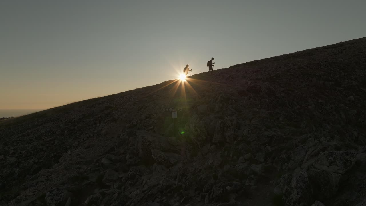una joven pareja caminando por husfjellet en senja, noruega, durante una impresionante puesta de sol de medianoche