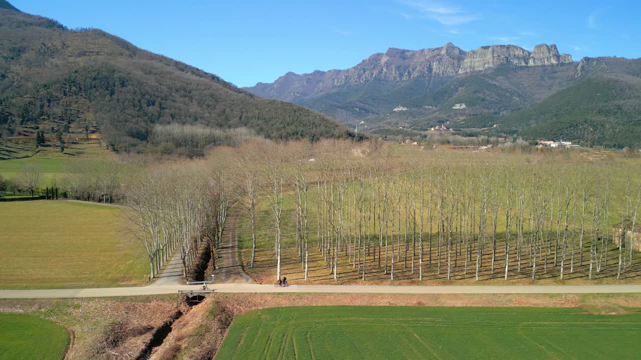 drone rastreando a un ciclista en un paisaje idílico con campos verdes cultivados y hermosas montañas al fondo