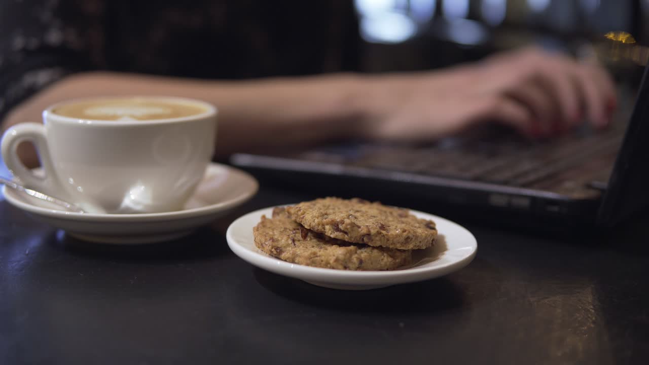 taza de café y coockies. mujer trabajando con computadora portátil en el fondo
