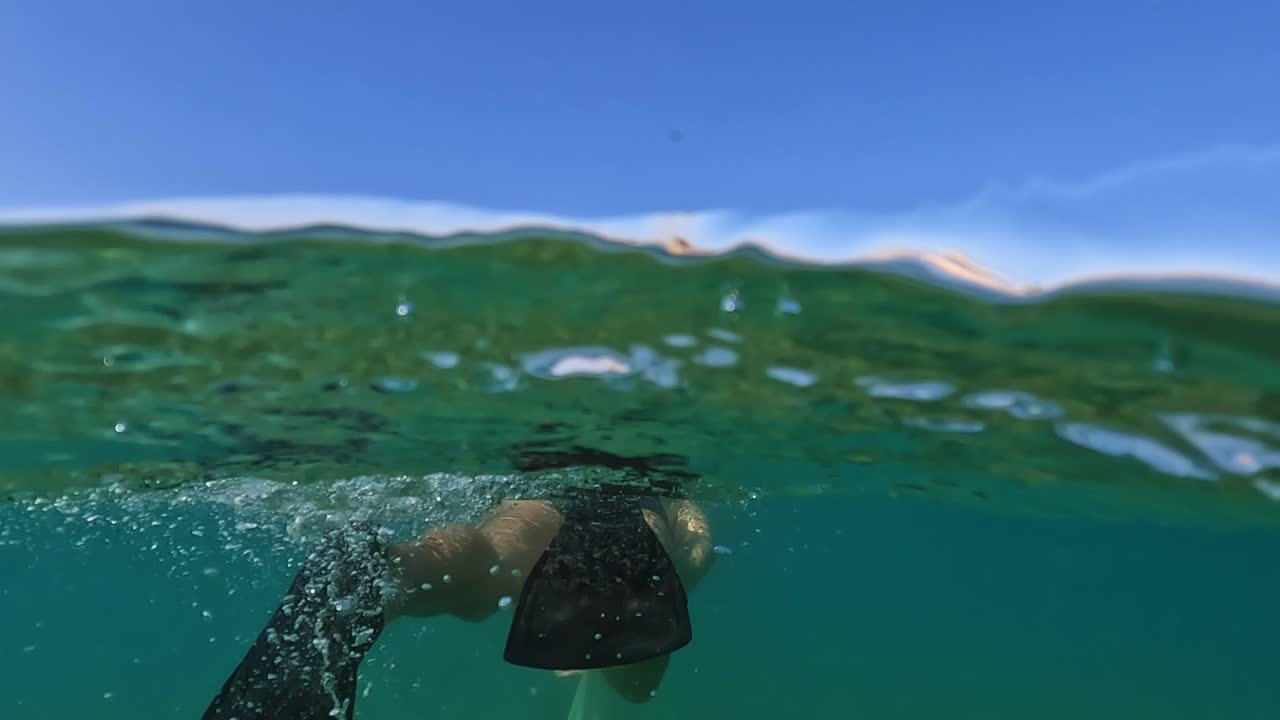 vista trasera medio submarina de un hombre adulto con máscara y snorkel amarillo nadando en el mar adriático azul con aletas de buceo a lo largo de plataformas de pesca trabocchi en abruzzo, italia