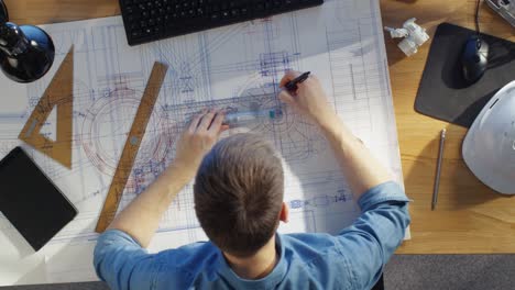 top view of a technical engineer working on his blueprints, drawing on plans. various drawing objects lying on his table.