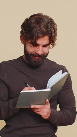 Thoughtful businessman making notes writing down thoughts with pen into diary on beige background