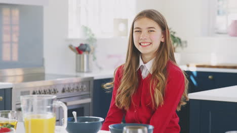 portrait of smiling teenage girl wearing school uniform in kitchen eating healthy breakfast