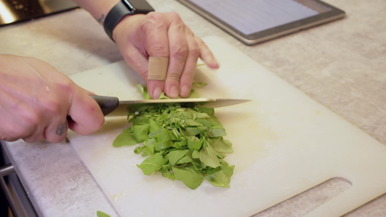 Tattooed woman chops baby arugula greens on white cutting board