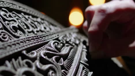 close-up of a hand examining intricate carvings on an ancient metal artifact