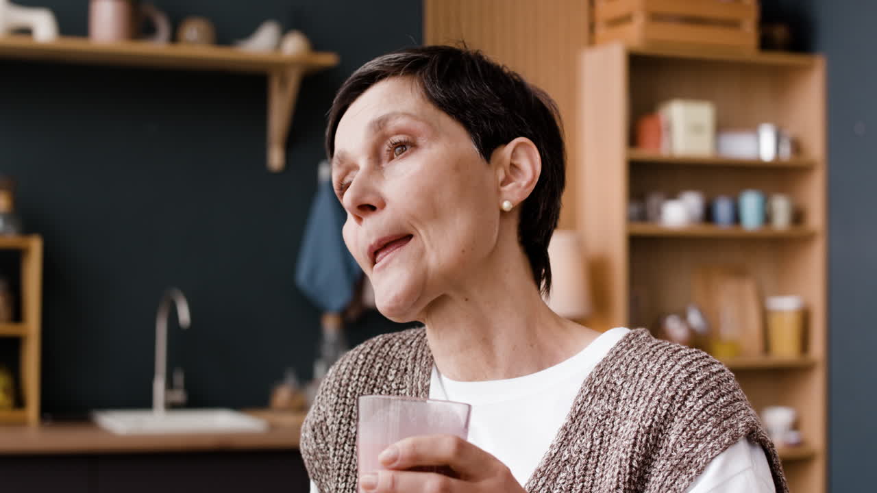 Middle-aged woman drinking a beverage in her kitchen