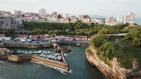 picturesque port des pêcheurs harbor in biarritz, boats moored inside seawall and city skyline, sainte-eugénie church, france. aerial drone