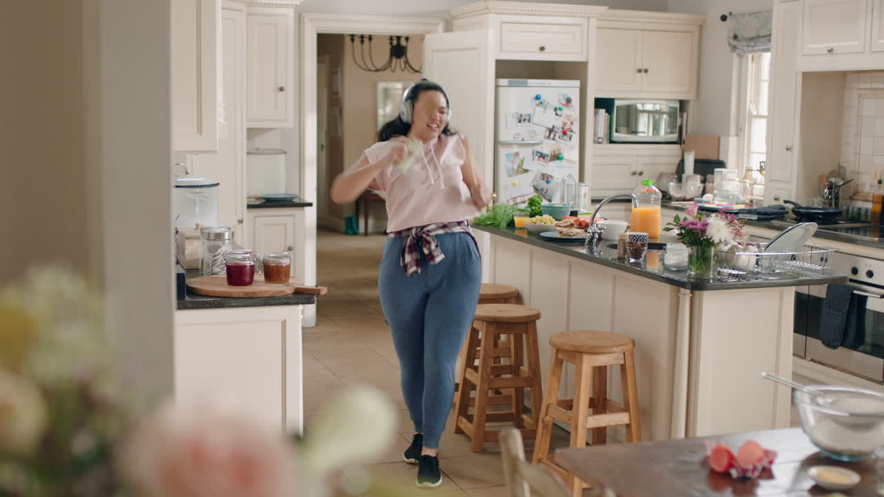 happy overweight teenage girl dancing in kitchen having fun celebrating weekend performing funny dance moves listening to music wearing headphones