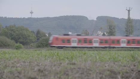 red deutsche bahn regio train moving swiftly through green fields on a cloudy day, slight motion blur