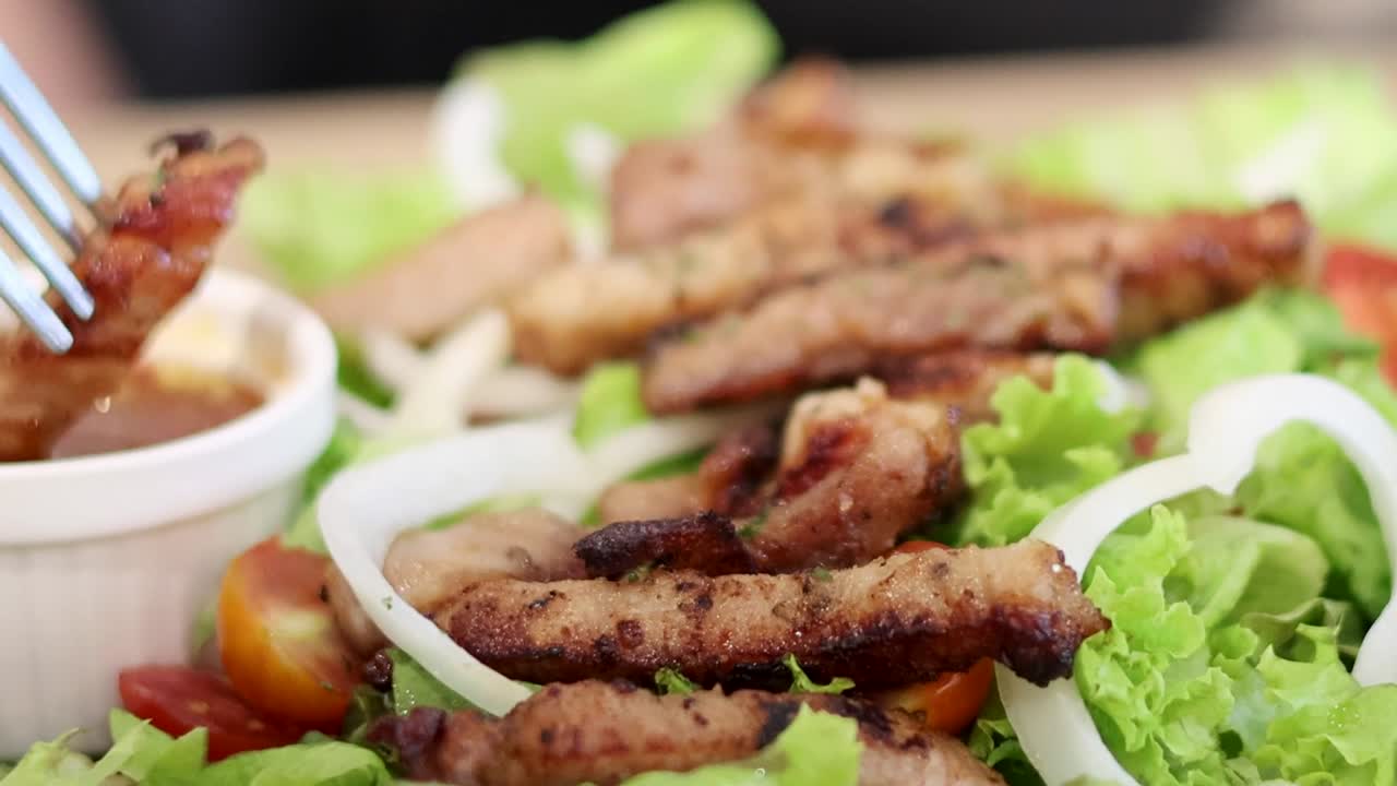 Close-up of grilled meat slices on fresh salad with a side of tangy dipping sauce.